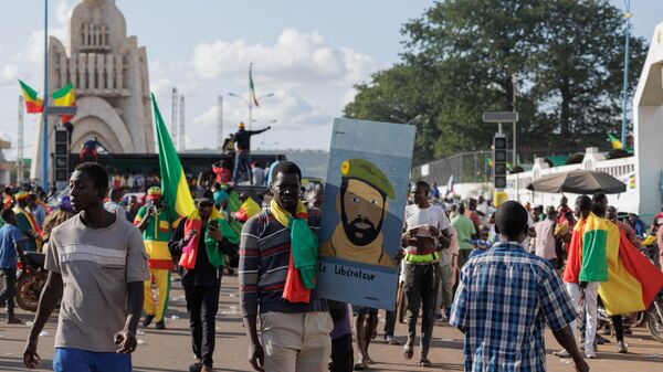 Attendees, including one (C) holding a board representing the Interim president of Mali and Junta leader, gather while holding Mali national flags during Mali’s Independence Day Celebrations and a march against United Nations Multidimensional Integrated Stabilization Mission in Mali (MINUSMA) at the Independence square in Bamako on September 22, 2022.  - Sputnik Africa