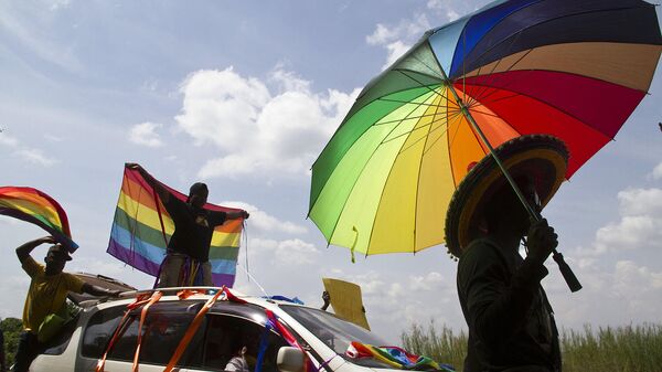 A person holds an umbrella bearing the colors of the rainbow flag as others wave flags during the the first gay pride rally since the overturning of a tough anti-homosexuality law, which authorities have appealed, in Entebbe, on August 9, 2014.   - Sputnik Africa