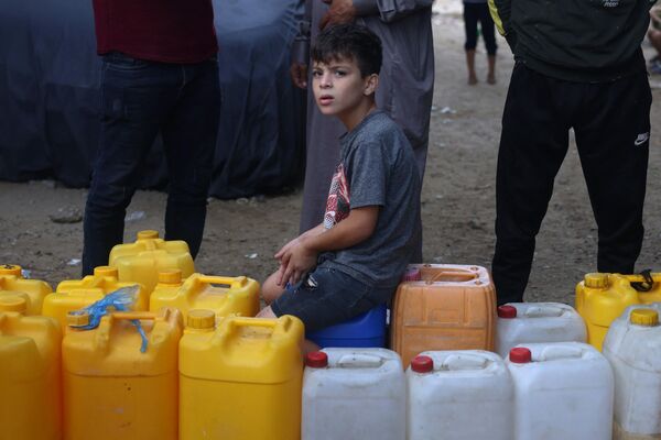 A young Palestinian sit on plastic jerrycans at a water filling point, in Rafah in the southern Gaza Strip on October 28, 2023, amid the ongoing battles between Israel and the Palestinian group Hamas.  - Sputnik Africa