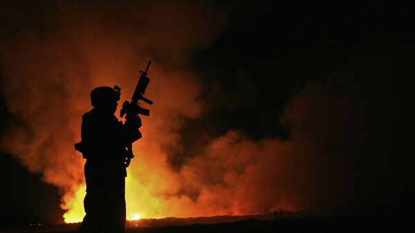 Sgt. Robert B. Brown from Fayetteville, N.C. with Regimental Combat Team 6, Combat Camera Unit watches over the civilian Fire Fighters at the burn pit as smoke and flames rise into the night sky behind him on May 25th, 2007. - Sputnik Africa