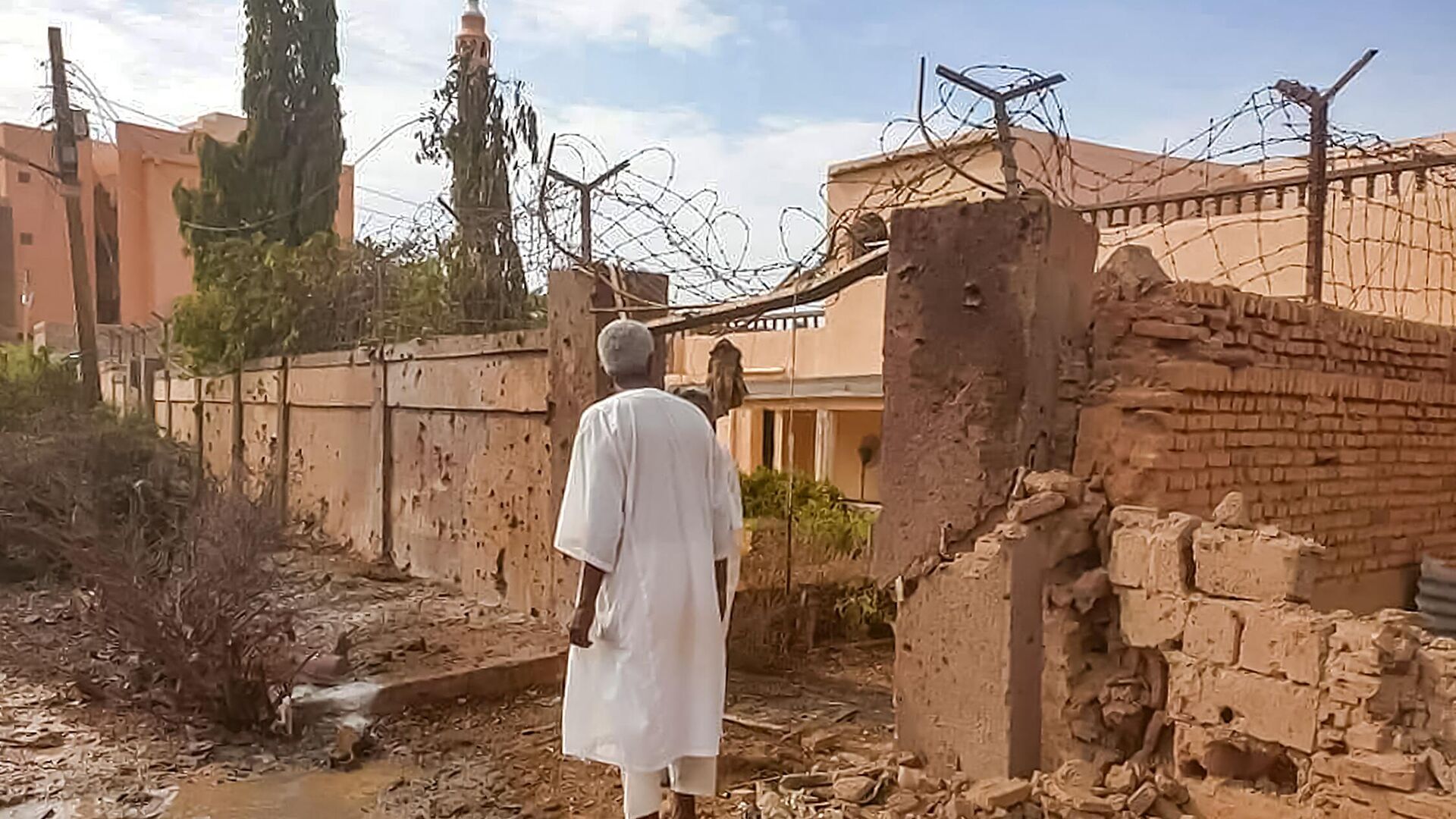 A man walks through rubble by a bullet-riddled fence with barbed-wire, in the aftermath of clashes and bombardment in the Ombada suburb on the western outskirts of Omdurman, the twin-city of Sudan's capital, on July 4, 2023. - Sputnik Africa, 1920, 21.11.2023