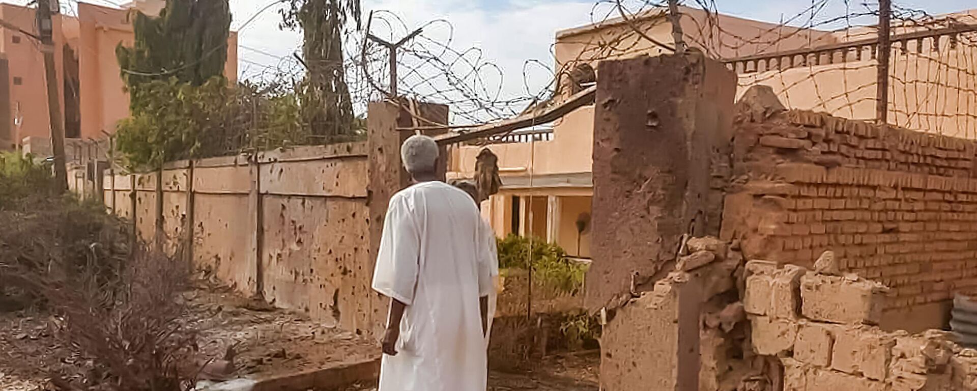 A man walks through rubble by a bullet-riddled fence with barbed-wire, in the aftermath of clashes and bombardment in the Ombada suburb on the western outskirts of Omdurman, the twin-city of Sudan's capital, on July 4, 2023. - Sputnik Africa, 1920, 21.11.2023