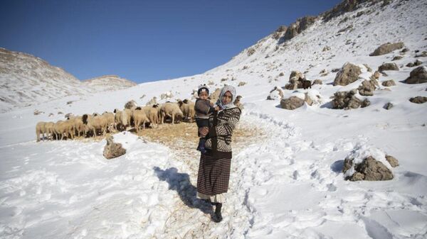Une femme porte son fils après avoir nourri les moutons dans un village du Moyen Atlas, au Maroc - Sputnik Afrique