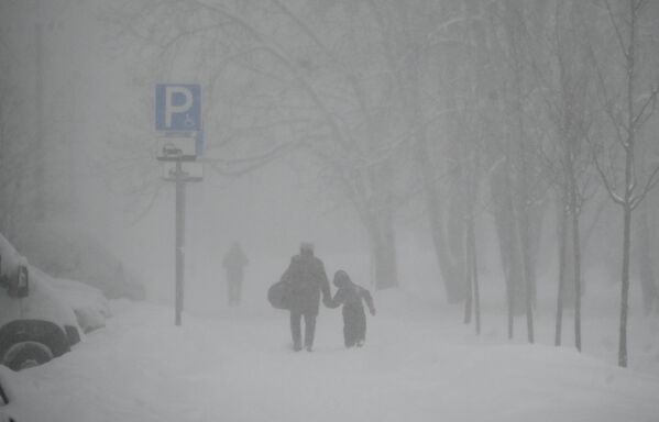 A man with a child on Maria Ulyanova Street during a heavy snowfall in the city. - Sputnik Africa