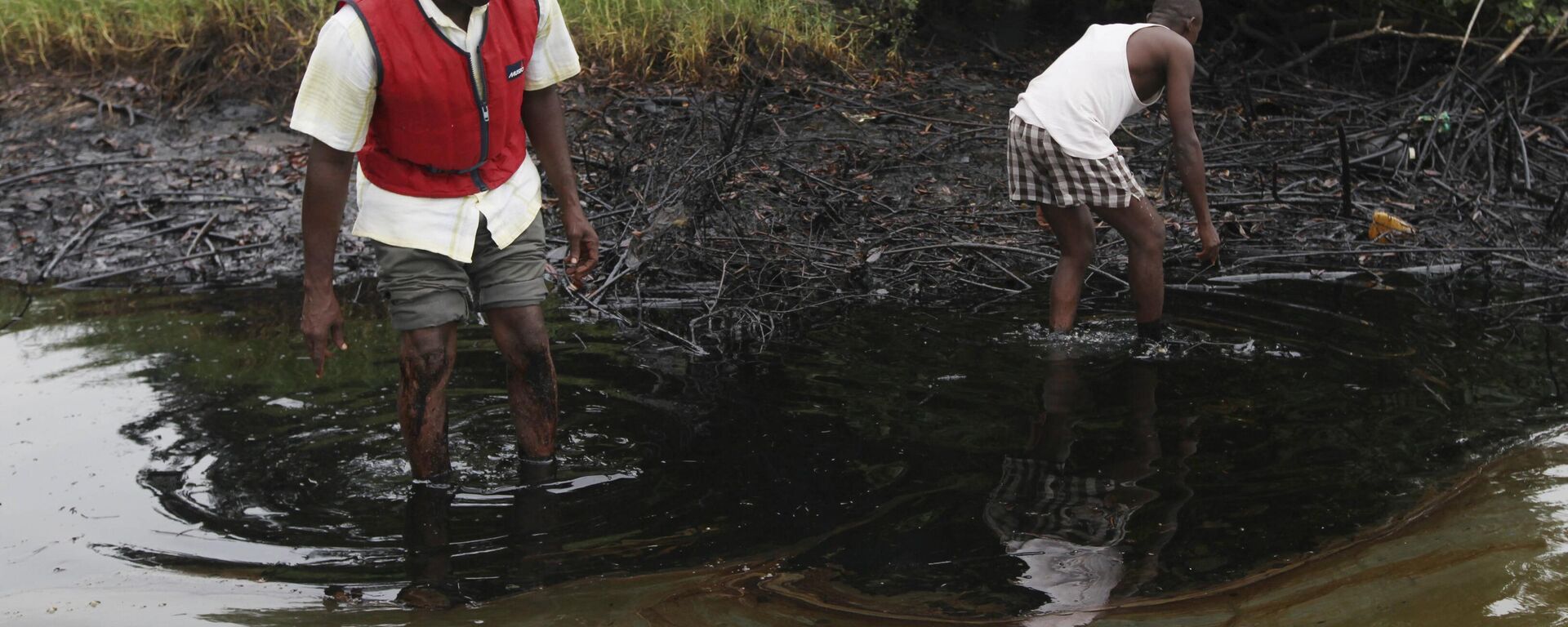 In this Sunday June 20, 2010 file photo, men walk in an oil slick covering a creek near Bodo City in the oil-rich Niger Delta region of Nigeria.  - Sputnik Africa, 1920, 04.12.2023