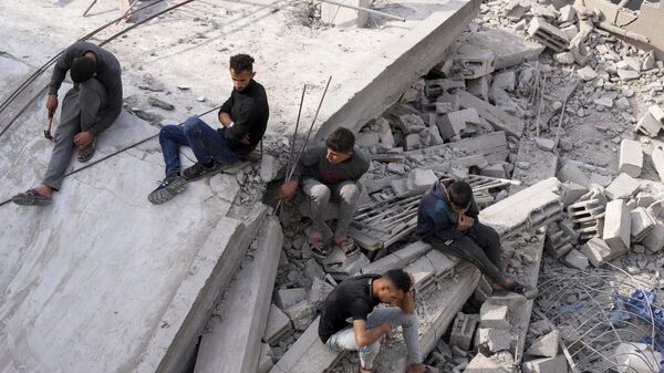 Palestinians sit by the building of the Al-Nadi family destroyed in the Israeli bombardment of the Gaza Strip in Nusseirat refugee camp, central Gaza Strip - Sputnik Africa
