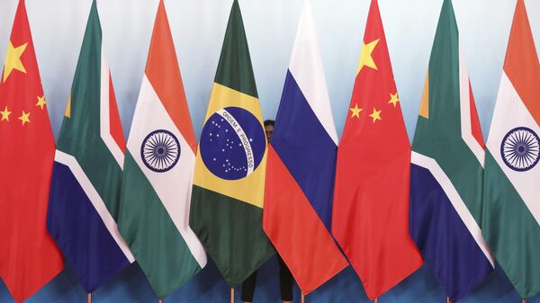Une employée se tient derrière les drapeaux nationaux du Brésil, de la Russie, de la Chine, de l'Afrique du Sud et de l'Inde pour les ranger avant une photo de groupe lors du sommet des BRICS au Centre international de conférence et d'exposition de Xiamen, le 29 septembre 2017. - Sputnik Afrique
