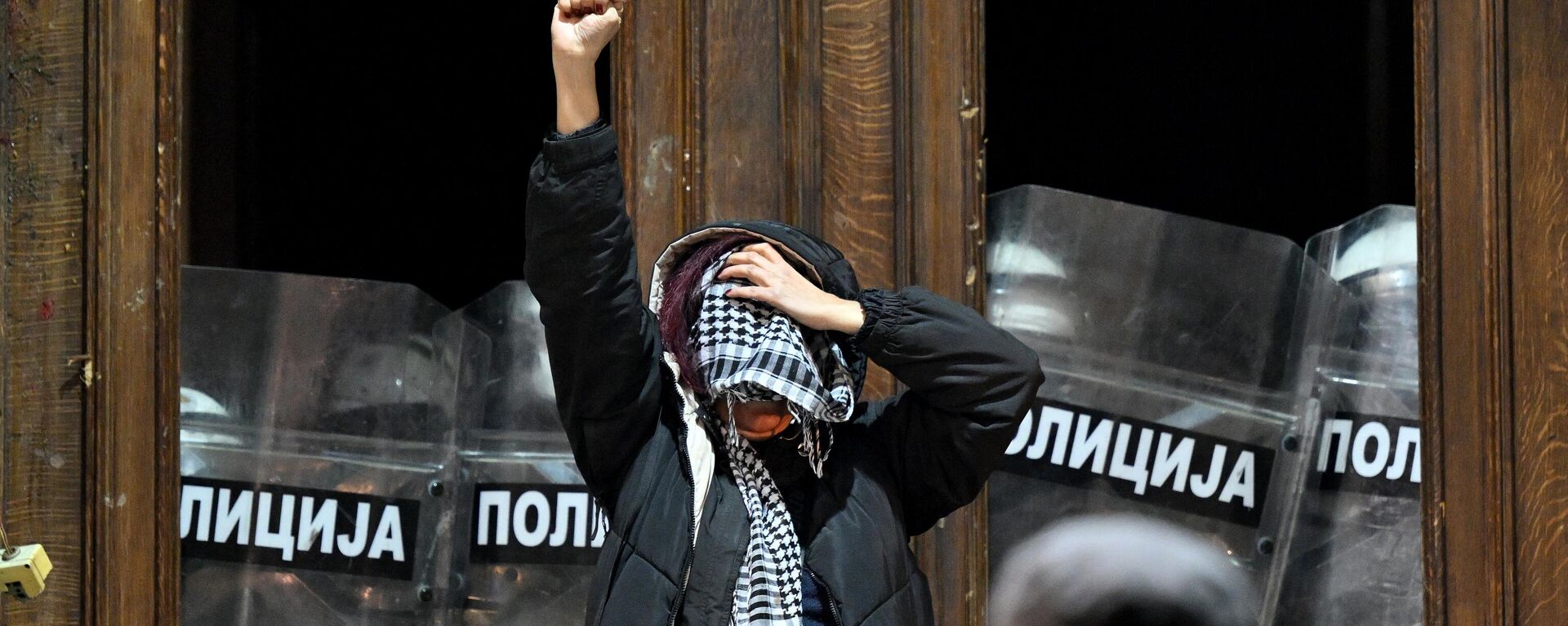 A protester raises a fist as police officers guard the entrance to the Belgrade's city council building during a demonstration in Belgrade, on December 24, 2023, a week after the parliamentary and local elections in Serbia. - Sputnik Africa, 1920, 25.12.2023