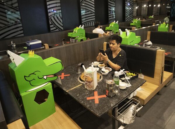 A customer uses a mobile phone while sitting with a cartoon dragon dolls the restaurant uses as space keepers for social distancing to help curb the spread of the coronavirus at shopping mall in Bangkok, Thailand, Monday, May 18, 2020.  - Sputnik Africa