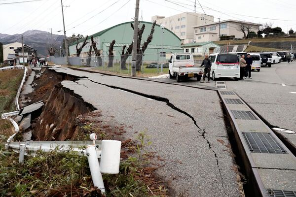 People stand next to large cracks in the pavement after evacuating into a street in the city of Wajima, Ishikawa prefecture on January 1, 2024, after a major 7.5 magnitude earthquake struck the Noto region in Ishikawa prefecture in the afternoon. - Sputnik Africa