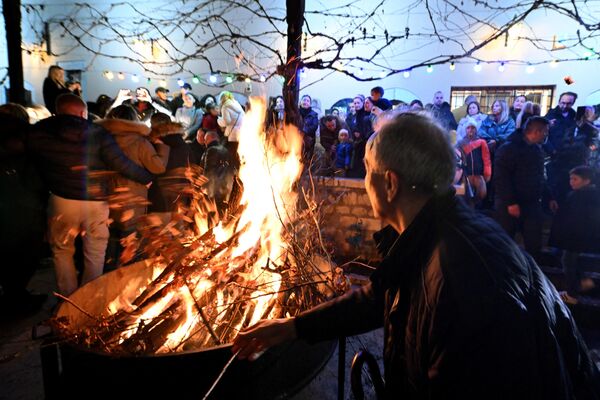 A man throws a branch into the fire as Sarajevo Orthodox Christians attend the annual bonfire of dried oak branches to mark the Orthodox Christmas Eve, at the Church of the Holy Archangels Michael and Gabriel, in Sarajevo, Bosnia and Herzegovina. - Sputnik Africa