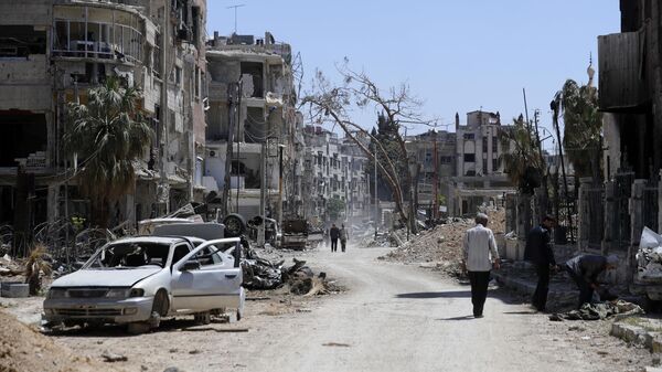 Syrians walk through destruction in the town of Douma, the site of a suspected chemical weapons attack, near Damascus, Syria, on April 16, 2018 - Sputnik Africa