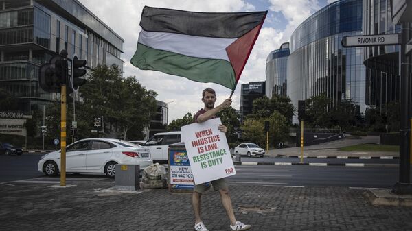 A pro Palestinian activist holds a banner and waves a Palestinian flag as he demonstrates following the International Court of Justice (ICJ) ruling of the case against Israel brought by South Africa in The Hague at the U.S. Consulate in Johannesburg on January 26, 2024. - Sputnik Africa