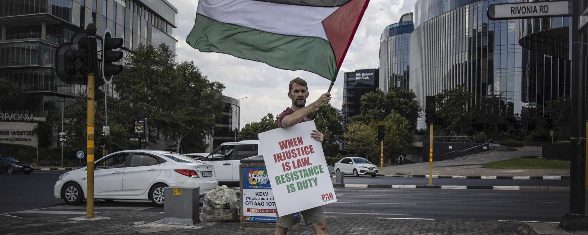 A pro Palestinian activist holds a banner and waves a Palestinian flag as he demonstrates following the International Court of Justice (ICJ) ruling of the case against Israel brought by South Africa in The Hague at the U.S. Consulate in Johannesburg on January 26, 2024. - Sputnik Africa, 1920, 27.01.2024