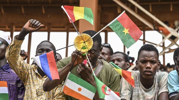A supporter of Niger's National Council for Safeguard of the Homeland (CNSP) holds national flags of Mali, Burkina Faso, Algeria, Niger and Russia as they gather at the general Seyni Kountche stadium in Niamey on Agust 26, 2023.  - Sputnik Africa