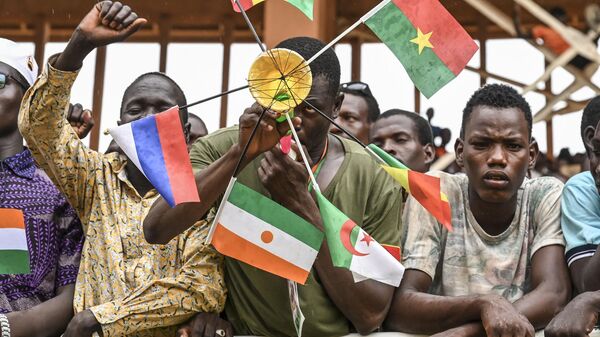 A supporter of Niger's National Council for Safeguard of the Homeland (CNSP) holds national flags of Mali, Burkina Faso, Algeria, Niger and Russia as they gather at the general Seyni Kountche stadium in Niamey on Agust 26, 2023.  - Sputnik Africa