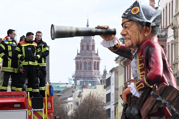 Firefighters stand on their vehicle as a carnival float depicting German Chancellor Olaf Scholz as a one-eyed pirate with a telescope passes by during the Shrove Monday carnival procession in Mainz, on Feb. 12, 2024, while the city&#x27;s Cathedral can be seen in the background. - Sputnik Africa