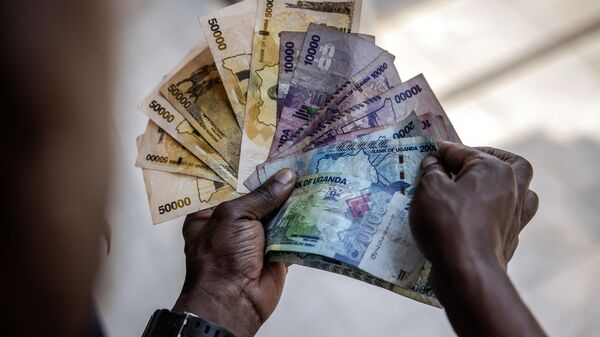 A man working for a forex bureau displays some Ugandan shilling notes for a costumer in downtown Kampala on January 20, 2024. - Sputnik Africa