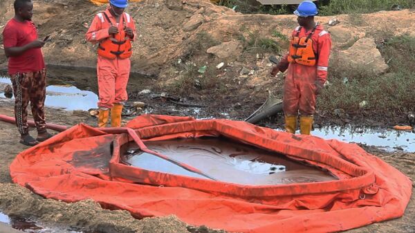 workers stand by a container to collect oil spill waste, in Ogoniland, Nigeria, June 16, 2023. An oil spill at a Shell facility in Nigeria has contaminated farmland and a river - Sputnik Africa