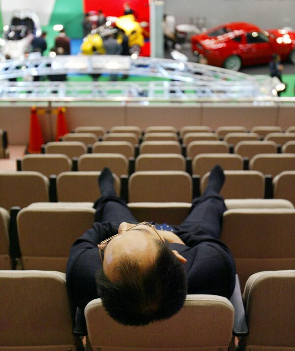 A Japanese businessman takes a nap on backs of chairs during the preview of Tokyo Motor Show in Makuhari, suburban Tokyo, 24 October 2003. - Sputnik Africa