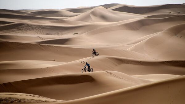 Competitors ride their bikes along sand dunes during the Stage 1 of the 14th edition of Titan Desert 2019 mountain biking race around Merzouga in Morocco on April 28, 2019. - Sputnik Africa