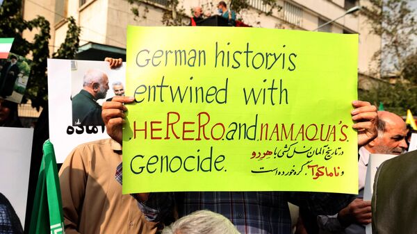 A protester holds up a sign reading in English and Persian German history is entwined with Herero and Namaqua's genocide, referring to an ethnic extermination and collective punishment campaign conducted by the German Empire in the early 20th century in the then-colony of German South West Africa (modern Namibia), during an anti-German demonstration condemning Germany's support of Berlin-based Iranian opposition TV stations and anti-government protests in Iran, outside the German embassy headquarters in Iran's capital Tehran on November 1, 2022. - Sputnik Africa