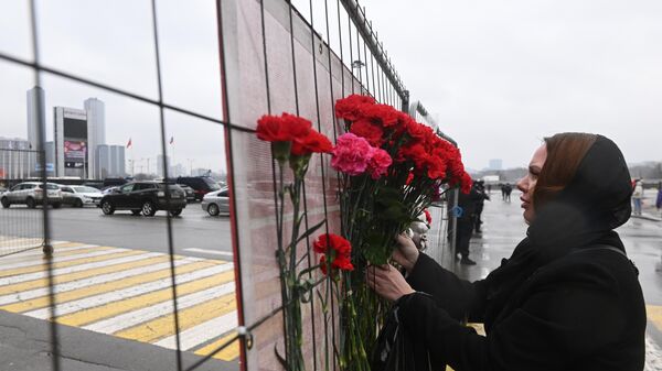 Люди несут цветы к зданию концертного зала Крокус Сити Холл, Россия - Sputnik Afrique