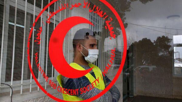 A worker of the Red Crescent Society stands at the entrance of a building hosting a hospital opened by the governor of Hebron and equipped with modern appliances, to receive patients affected by the coronavirus Covid-19 in the village of Halhul, near the city of Hebron in the occupied West Bank, on March 15, 2020. - Sputnik Africa