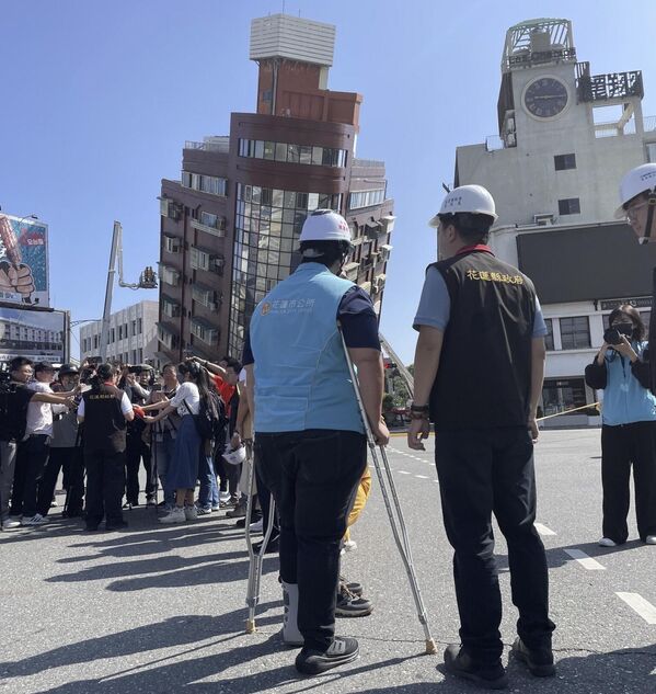 Government workers and journalists are seen near firefighters working near a leaning building in the aftermath of an earthquake in Hualien, eastern Taiwan.  - Sputnik Africa