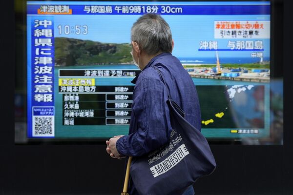 A person stands along a sidewalk to watch a TV showing a breaking news on tsunami for Okinawa region in Tokyo. Japan issued tsunami alerts on Wednesday after a strong quake near Taiwan. (AP Photo/Eugene Hoshiko) - Sputnik Africa