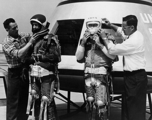 Three NASA personnel suited in space-flight restraining gear prepare to climb aboard the Apollo Spacecraft April 6, 1962. This preliminary mock-up model was placed on display April 6.13ft wide and 12ft high, this command module was the most complex manned flight device ever designed and built for earth orbit and lunar landing. - Sputnik Africa