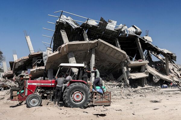 People ride on a tractor picking up salvaged items from a damaged building in Khan Yunis on April 7, 2024 after Israel pulled its ground forces out of the southern Gaza Strip. - Sputnik Africa