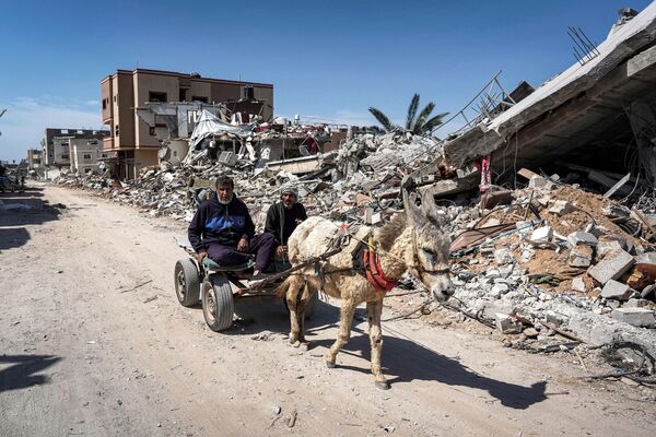 Two men sit in a donkey-drawn cart moving past the rubble of a destroyed building in Khan Yunis on April 7, 2024 after Israel pulled its ground forces out of the southern Gaza Strip. - Sputnik Africa