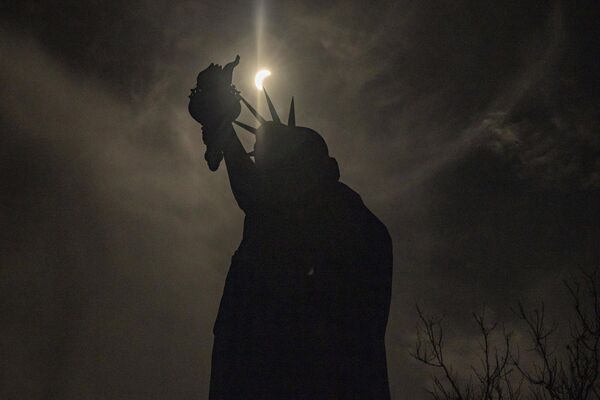 The moon partially covers the sun behind the Statue of Liberty during the solar eclipse on Liberty Island, Monday, April 8, 2024, in New York.  - Sputnik Africa