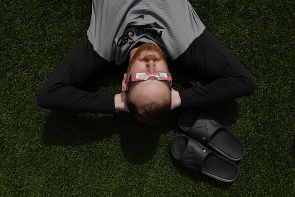 Chicago White Sox pitcher Steven Wilson lays in the grass outside the dugout and looks up through special glasses during a total solar eclipse, at Progressive Field in Cleveland on Monday, April 8, 2024, before the Cleveland Guardians home opener baseball game against the White Sox.  - Sputnik Africa