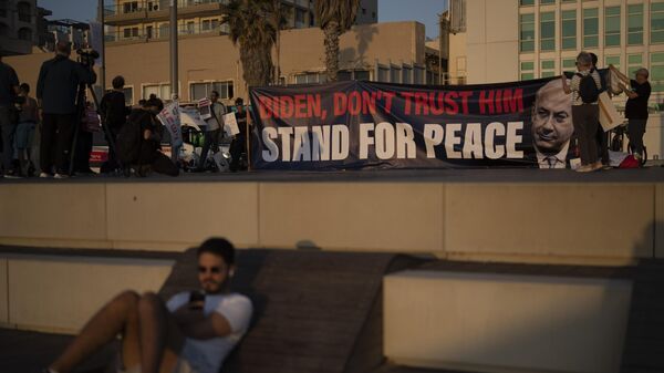People hold a banner referring to the U.S. president Joe Biden to not trust in the Israeli Prime Minister Benjamin Netanyahu as they demonstrate demanding the end of the Israel-Hamas war with a regional peace agreement outside of the U.S. Embassy Branch Office in Tel Aviv, Monday, April 15, 2024. - Sputnik Africa