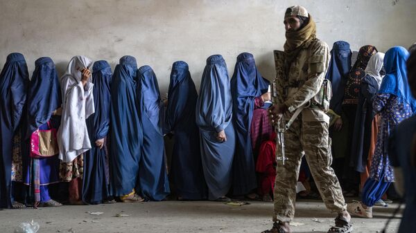 A Taliban fighter stands guard as women wait to receive food rations distributed by a humanitarian aid group, in Kabul, Afghanistan - Sputnik Africa