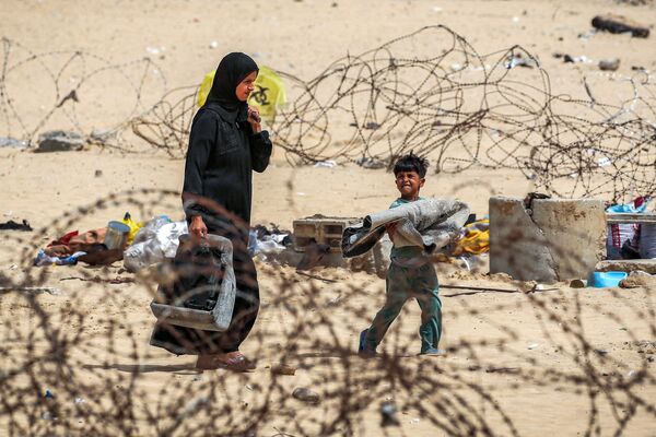 A woman and boy walk with belongings past barbed-wire fences as they flee from Rafah in the southern Gaza Strip on May 11, 2024 amid the ongoing conflict in the Palestinian territory between Israel and Hamas. - Sputnik Africa