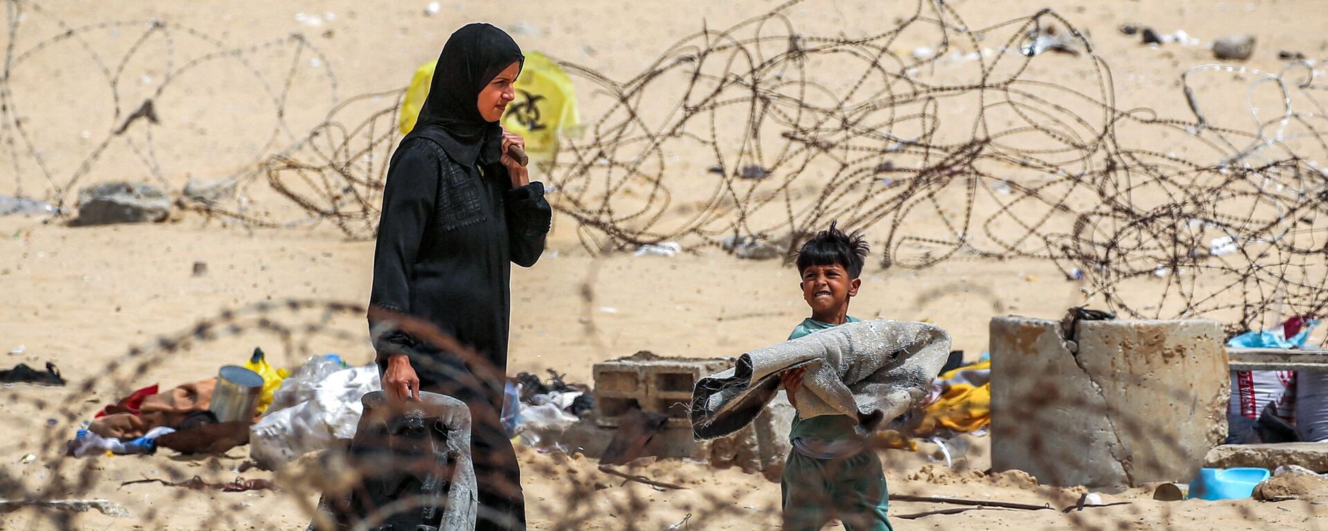 A woman and a boy are walking with their belongings past fences made of barbed wire as they flee from Rafah in the southern Gaza Strip. - Sputnik Africa, 1920, 27.05.2024