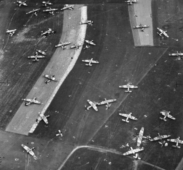 Oblique photographic-reconnaissance vertical, taken from 800 feet, showing part of Landing Zone &#x27;N&#x27;, north of Ranville, Normandy, on the day following Operation MALLARD: the airborne landing of 6th Airlanding Brigade and the Airborne Armoured Reconnaissance Regiment in the evening of 6 June 1944. Airspeed Horsa troop-carrying gliders and one damaged GAL Hamilcar tank-carrying glider (lower right) litter this part of the LZ close to the Ranville-Salanelles road. - Sputnik Africa