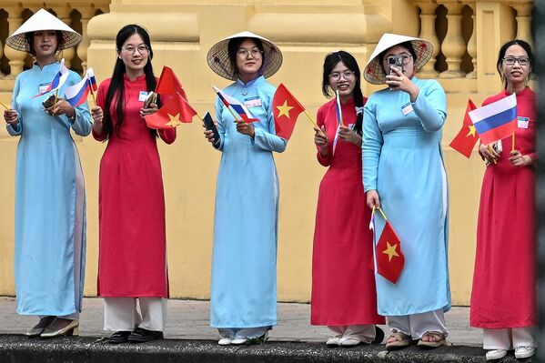 Women wearing traditional Vietnamese &quot;Ao Dai&quot; dresses wave Vietnamese and Russian national flags while waiting for the arrival of Russia&#x27;s President Vladimir Putin outside the Presidential Palace in Hanoi on June 20, 2024. - Sputnik Africa