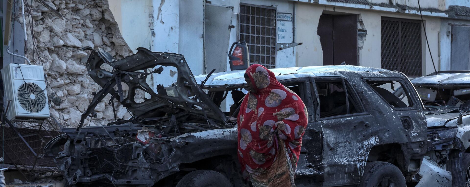 A woman walks past debris and destruction at a cafe in Mogadishu on July 15, 2024 following a car bomb blast where five people were killed where football fans were watching the Euro 2024 final late on July 14, 2024.  - Sputnik Africa, 1920, 03.08.2024