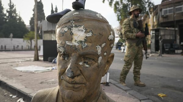 An opposition fighter in military uniform stands next to a broken bust of the late Syrian President Hafez Assad, with a pair of shoes placed on top, at a checkpoint in Damascus, Syria, Wednesday, Dec. 11, 2024. - Sputnik Africa