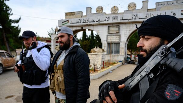 Islamist rebels of the Hayat Tahrir al-Sham (HTS) stand guard at the entrance of the first abandoned military base that reads Our Leader Forever - Hafez al-Assad on December 11, 2024. - Sputnik Africa