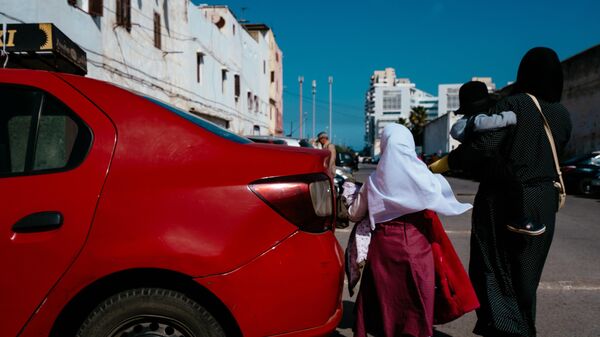 Mother and her kids walking by a parked red car on a street in Hassan II mosque neighbourhood. - Sputnik Africa