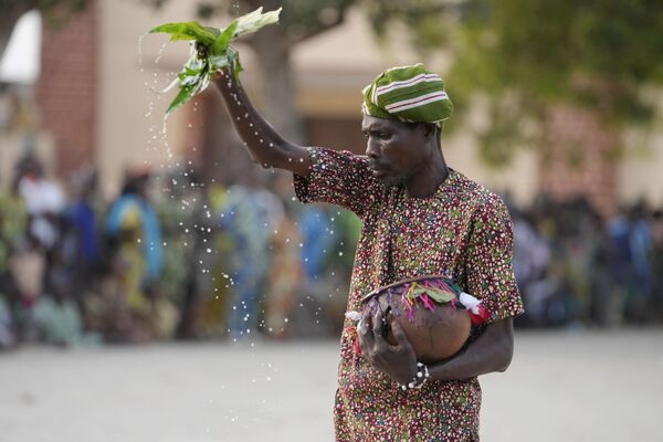 A man sprinkles water as Zangbeto masquerades the traditional Voodoo guardians of the night performing ahead of the annual Voodoo Festival, Ouidah, Benin, Jan. 9, 2025. - Sputnik Africa