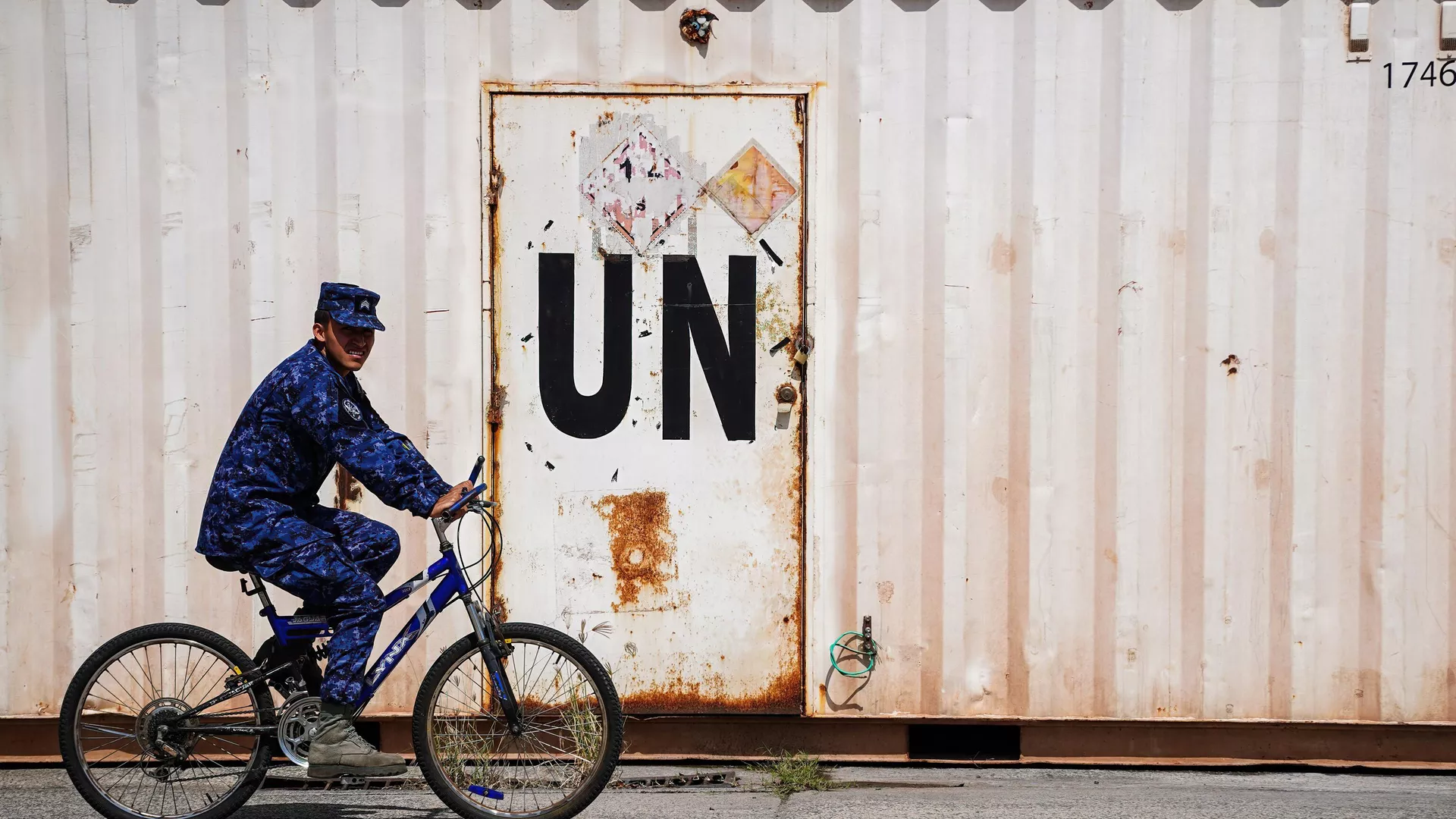 A soldier rides a bicycle next to a container with a UN label before deployment to Haiti as part of a UN Multinational Security Support Mission, in Ilopango.