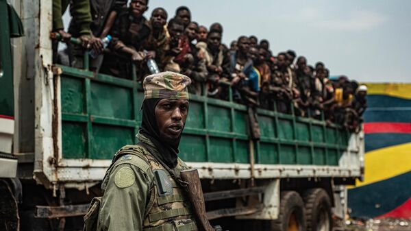 An M23 fighter stands in the foreground as detained FARDC soldiers are loaded onto trucks, to be taken to an unknown location, as an estimated 2400 Congolese (FARDC) soldiers surrendered en masse to M23 forces at the Stade de l'Unite on January 30, 2025 in Goma, Democratic Republic of Congo.  - Sputnik Africa