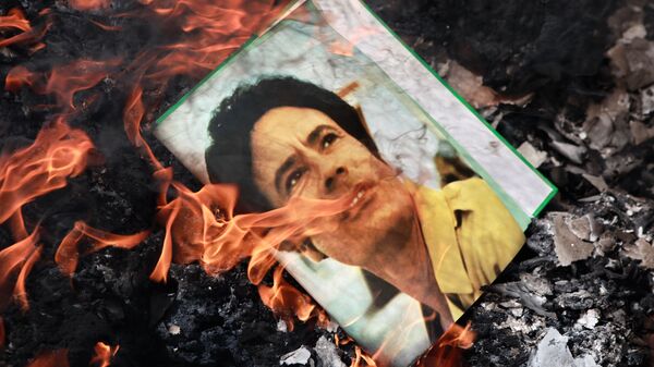 A portrait of Muammar Gaddafi burning in a fire. - Sputnik Africa