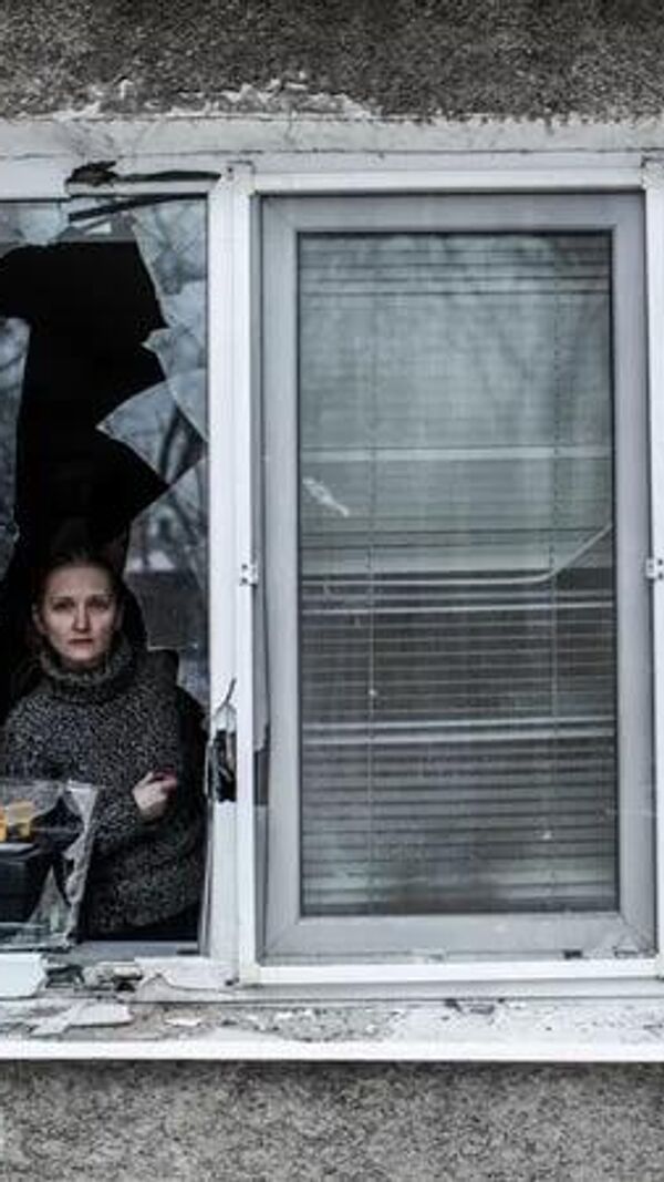 Une femme regarde à travers une fenêtre brisée de son appartement après qu'il a été touché par l'artillerie ukrainienne dans le quartier de Voroshilovski, dans le centre de Donetsk. - Sputnik Afrique